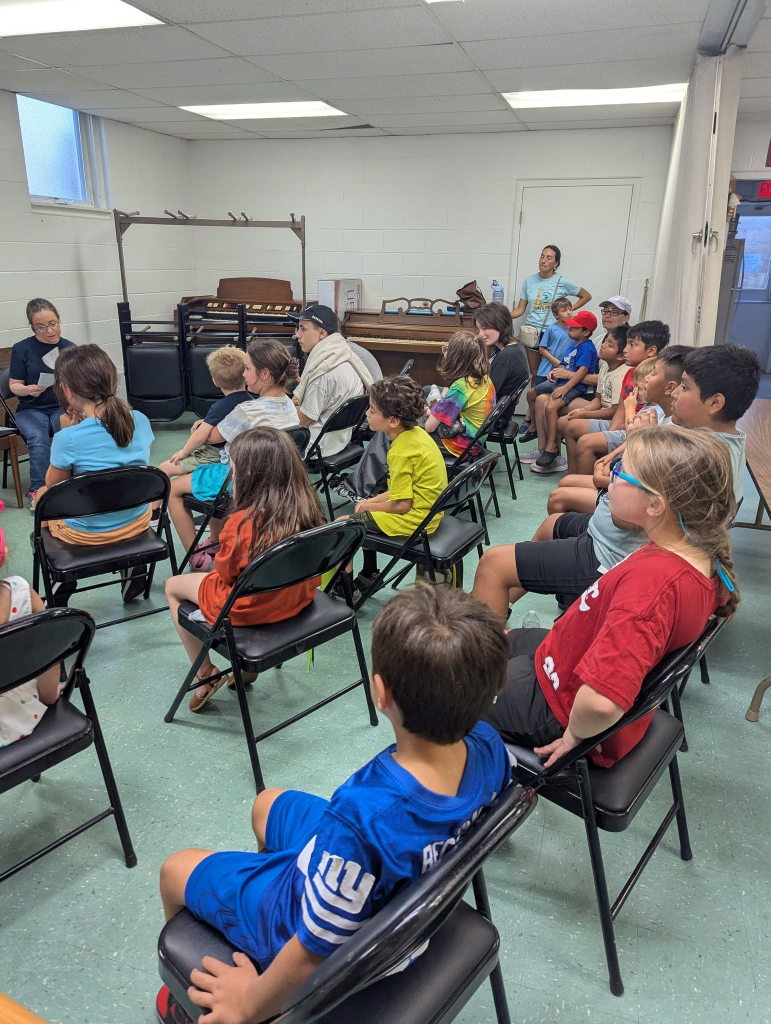 Children attending an indoor church activity session seated on chairs.