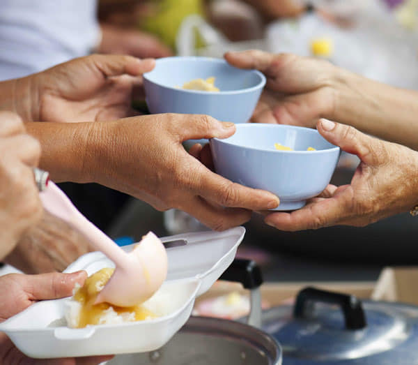 Volunteers serving food into bowls during a community meal.