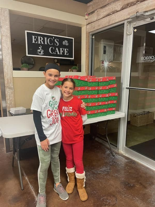 Two children standing beside stacked food donation boxes at a community collection point.