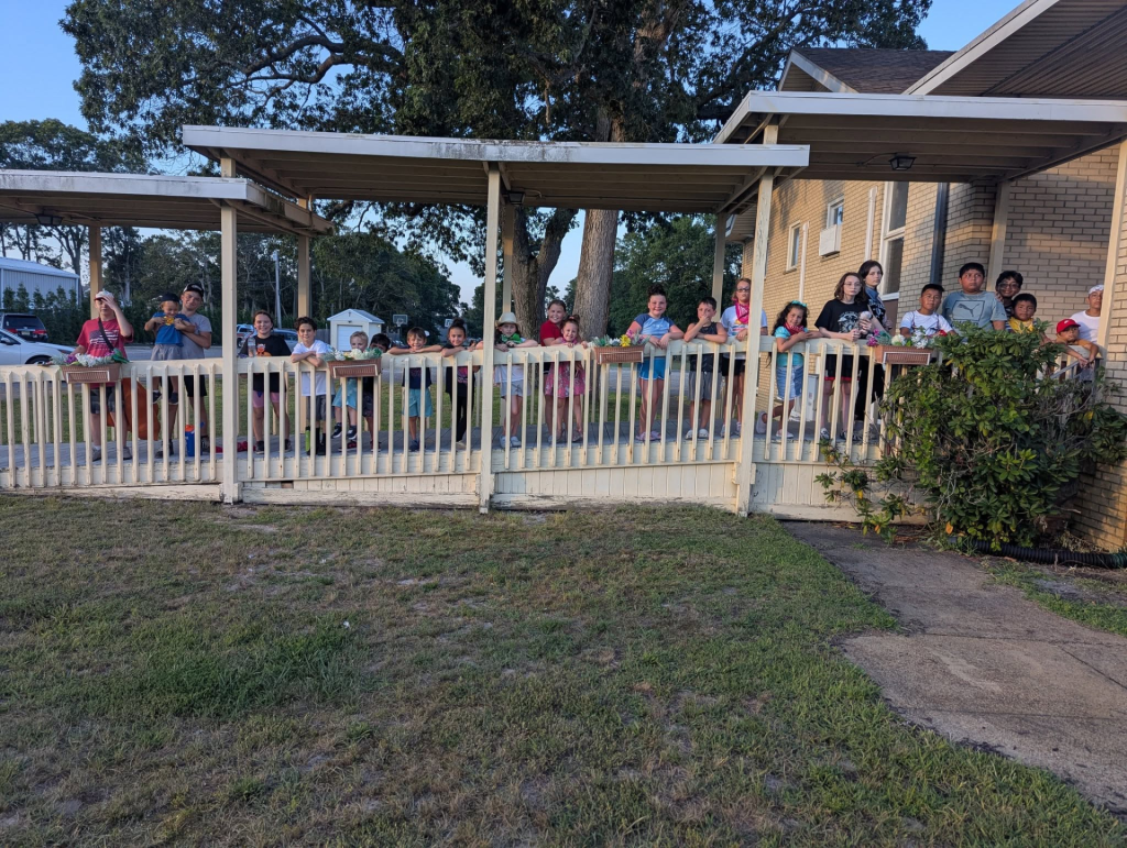 Outdoor church gathering under a covered pavilion with families seated.